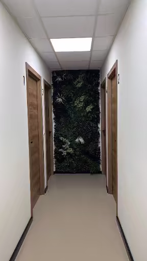 Pasillo de consultas con puertas numeradas y pared vegetal al fondo en Vórtice Pádel Club